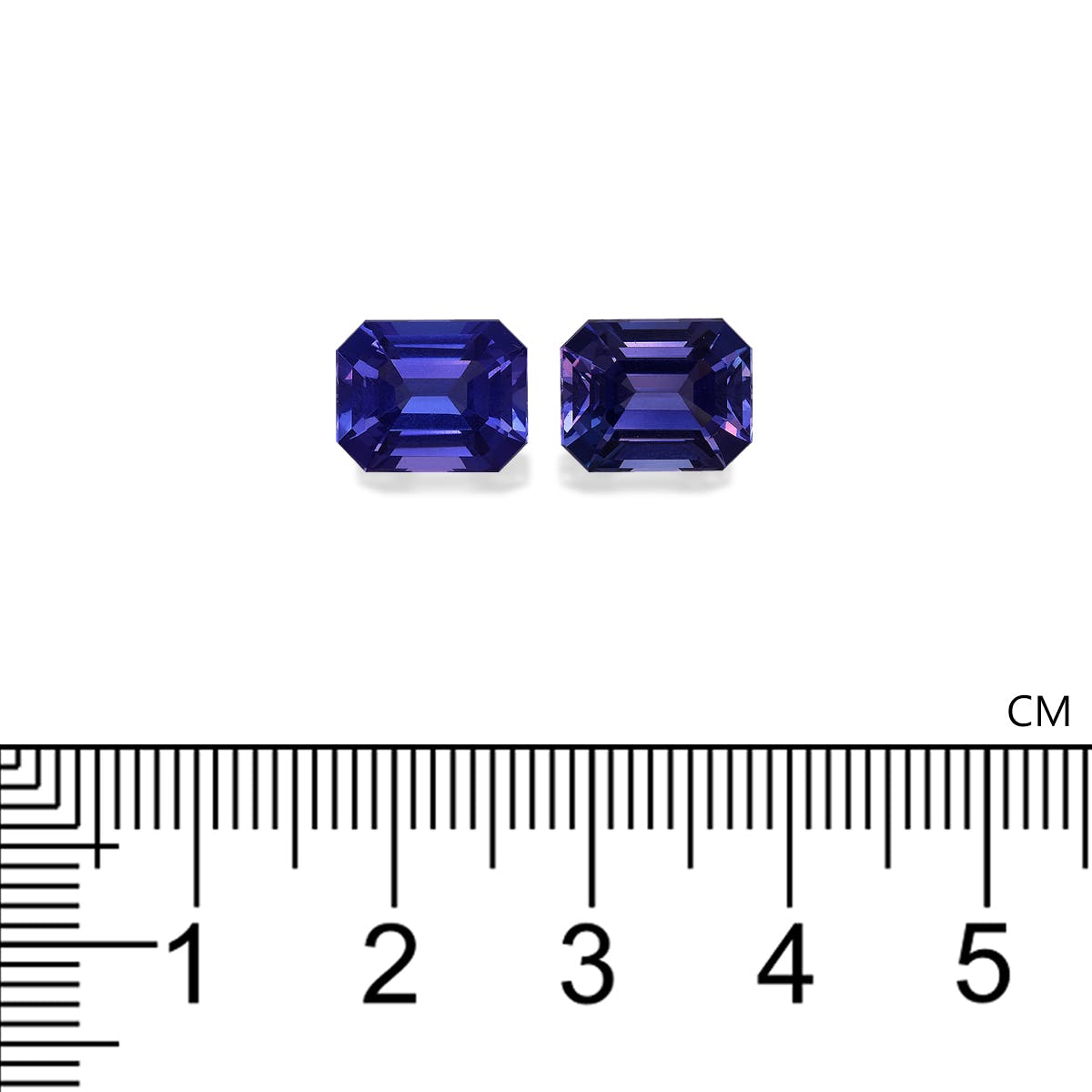 Deux petites pierres précieuses bleu foncé, rectangulaires et facettées, étiquetées Tanzanite · 6,9 ct par Bonnot Paris, sont placées côte à côte au-dessus d'une règle marquée en centimètres, indiquant qu'elles mesurent un peu plus de 1 cm de large.