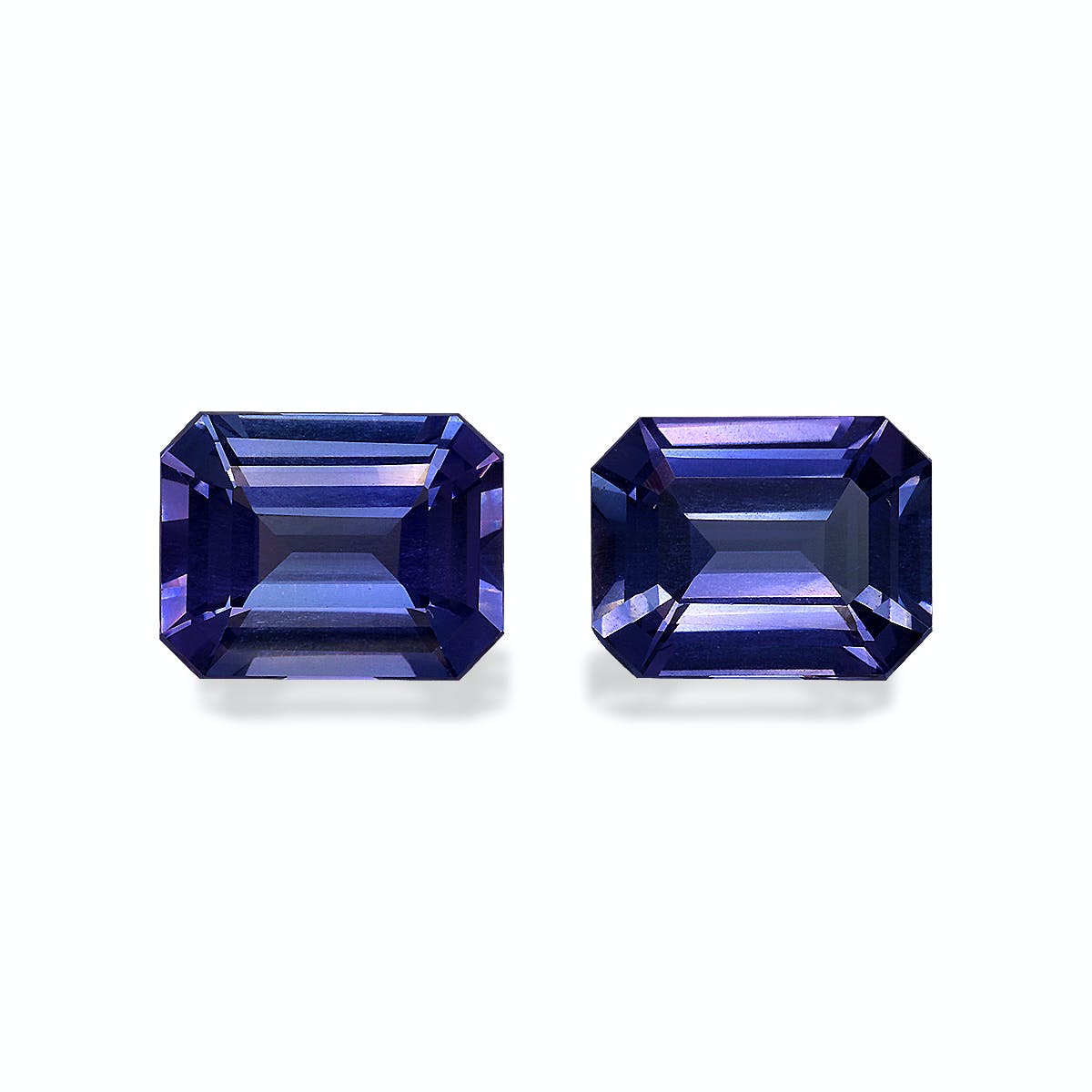 Deux pierres précieuses Tanzanite rectangulaires taille émeraude, de 5,82 ct chacune par Bonnot Paris, affichent une couleur bleu profond avec des facettes qui reflètent la lumière pour mettre en valeur des nuances de bleu et des touches de violet sur un fond clair.