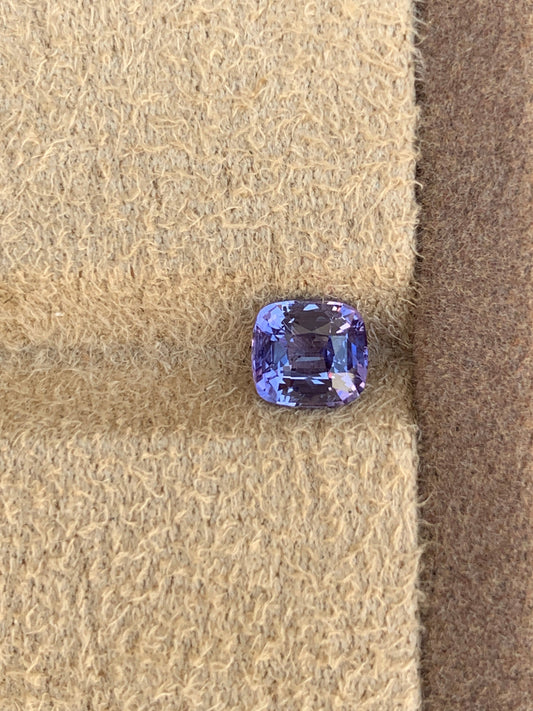 Le Saphir Violet • 1,62ct de Bonnot Paris, une gemme taille coussin du Sri Lanka, est élégamment présenté sur un fond texturé beige pour mettre en valeur son éclat et ses facettes.