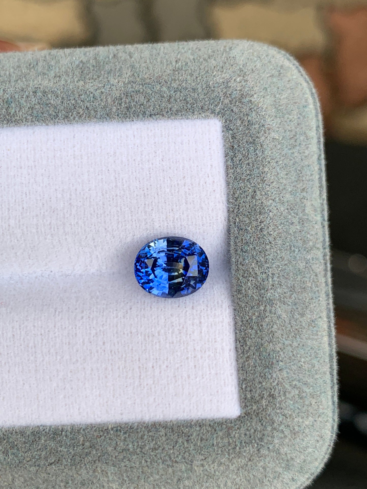Un gros plan sur le Saphir Bleu • 2,10ct de Bonnot Paris révèle une pierre précieuse de forme ovale affichant des nuances de bleu scintillantes sur un fond blanc et gris.