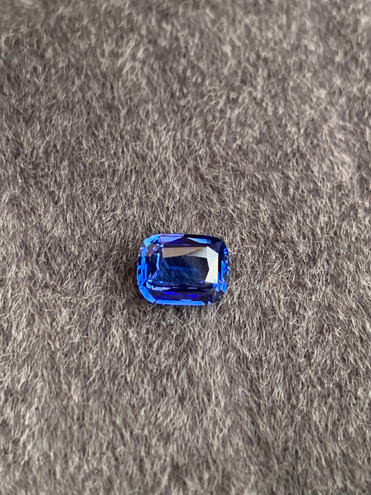 Le Saphir Bleu • 1,57ct de Bonnot Paris repose élégamment sur un tissu gris texturé, faisant écho à l'attrait exotique d'une pierre précieuse sri-lankaise avec ses surfaces facettées.