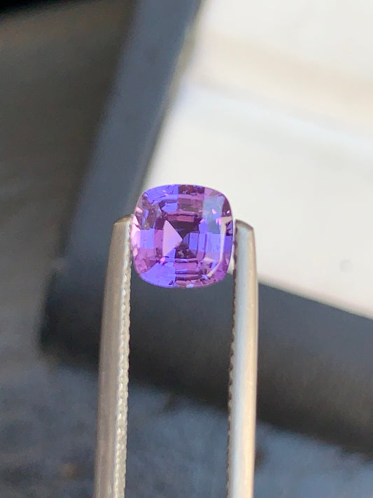 Gros plan sur la pierre précieuse Saphir Violet de Bonnot Paris de 1,5 carat, taille coussin et maintenue par une pince métallique. Cette magnifique pierre scintille de clarté sur un fond flou, évoquant le charme des trésors cachés de Madagascar.