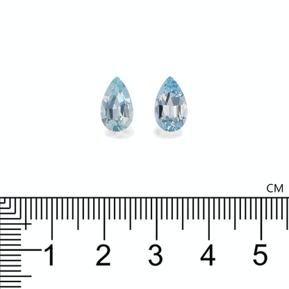 Deux pierres précieuses bleues en forme de poire, Bonnot Paris Aigue-Marine · 2,72 ct, sont placées côte à côte avec une règle indiquant leur hauteur de près de 2 cm, sur un fond blanc pour exsuder la sophistication et l'élégance.