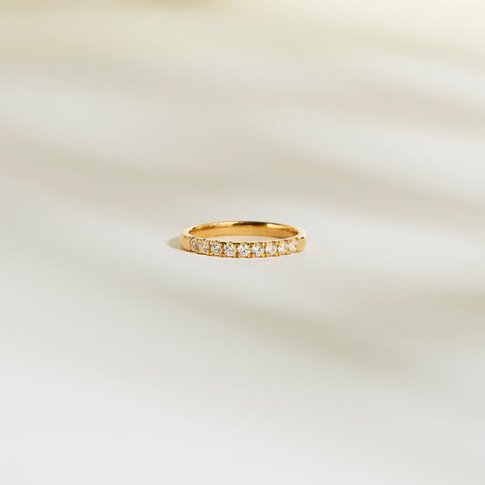 L'Alliance La Discrète de Bonnot Paris arbore une bague en or sertie de petits diamants naturels scintillants. Son design taille rond-brillant, d'une élégante simplicité, capte magnifiquement la lumière sur un fond clair et légèrement flou.