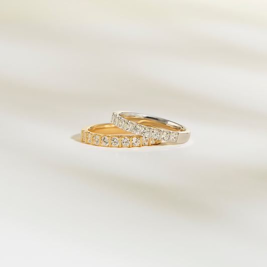 Les bagues Alliance La Majestueuse de Bonnot Paris, l'une en or et l'autre en argent, arborent des diamants brillants sur une surface douce et claire. Le fond légèrement flouté rehausse le luxe serein de la couleur clarté G/H SI.