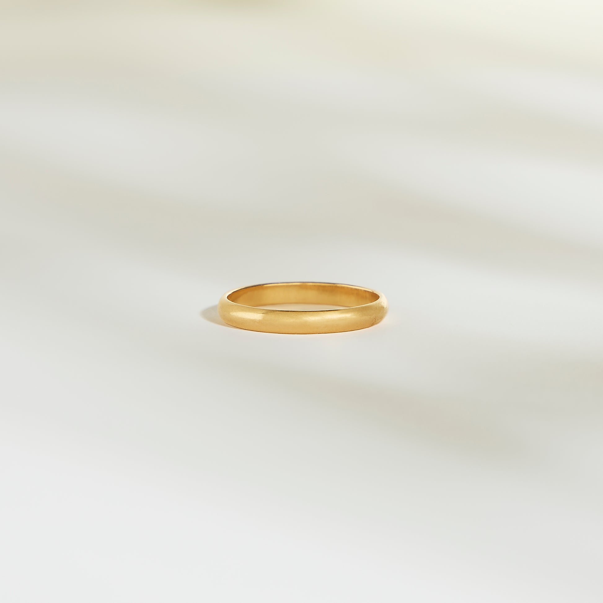 L'Alliance L'Authentique, un simple anneau en or signé Bonnot Paris, repose sur une surface pâle et légèrement éclairée. Les ombres subtiles qui l'entourent créent une atmosphère calme et élégante.
