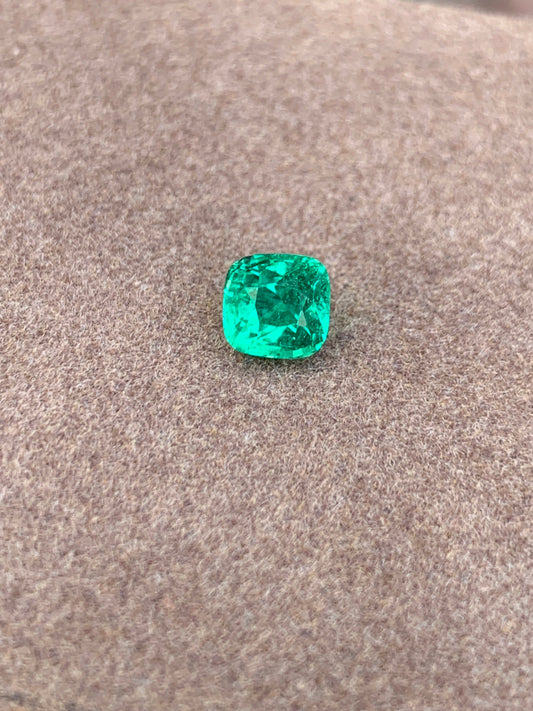 L'Émeraude taille coussin • 1,15ct de Bonnot Paris met en valeur sa teinte verte lumineuse sur une surface brune douce et texturée, reflétant magnifiquement la lumière de ses facettes.