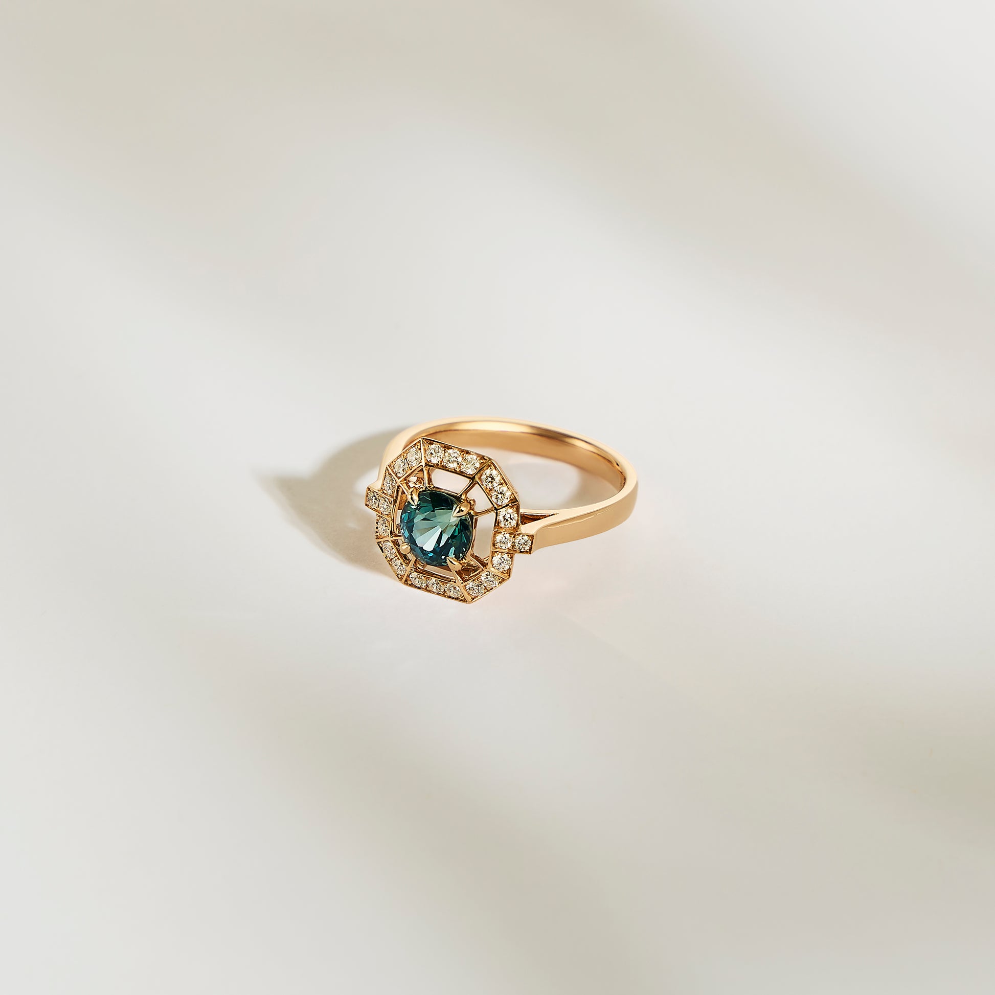 La Bague Saphir Teal • 1,16ct de Bonnot Paris présente un large saphir bleu sarcelle entouré de diamants blancs étincelants, élégamment présenté sur un fond doux et clair.