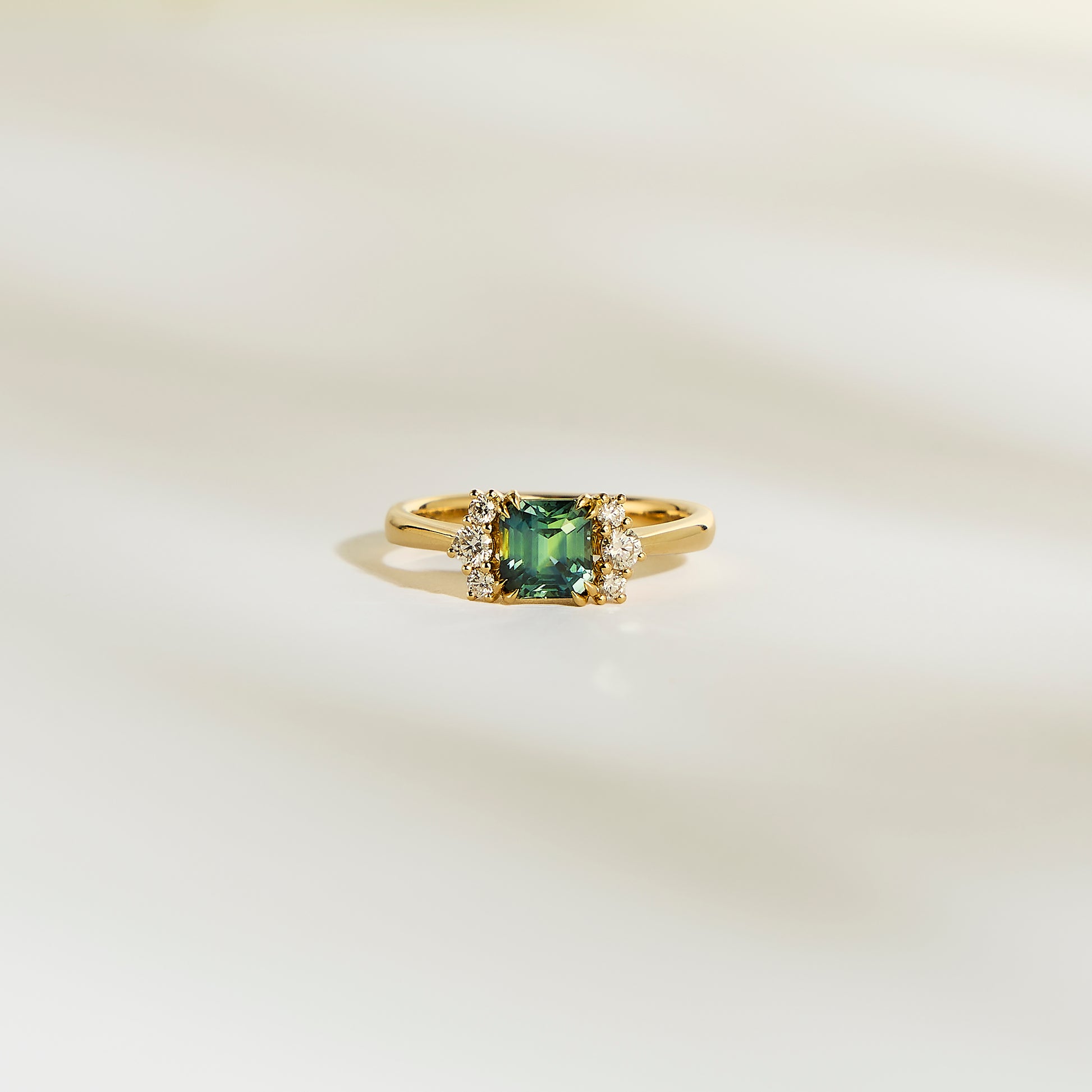La Bague Bonnot Paris Saphir Teal • 1,24 ct présente une pierre précieuse sarcelle carrée flanquée de petits diamants blancs étincelants sur une bande lisse et de couleur claire.