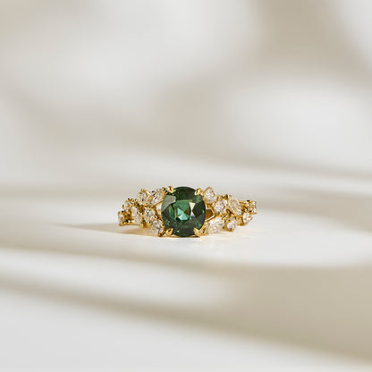 La Bague Saphir Teal • 2,07ct de Bonnot Paris, une bague en or avec un centre en saphir bleu sarcelle saisissant entouré de pierres claires, repose élégamment sur une surface crème doucement éclairée avec des ombres douces.