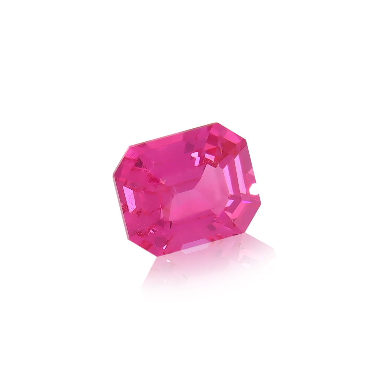 Un Spinelle Mahenge rose vibrant • 2,15 ct de Nascendi Paris, doté d'une taille émeraude à multiples facettes qui reflètent la lumière, repose sur une surface blanche brillante, projetant un petit reflet et incarnant l'élégance des bijoux sur mesure.
