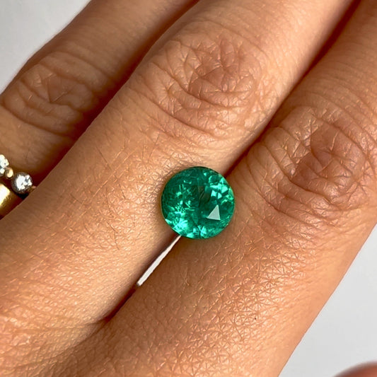 Une main ornée d'une bague en or uni et sertie de diamants équilibre l'Émeraude de Colombie Bonnot Paris • 1,91 ct au majeur, sa clarté exceptionnelle étant mise en valeur sur un fond doux et neutre.
