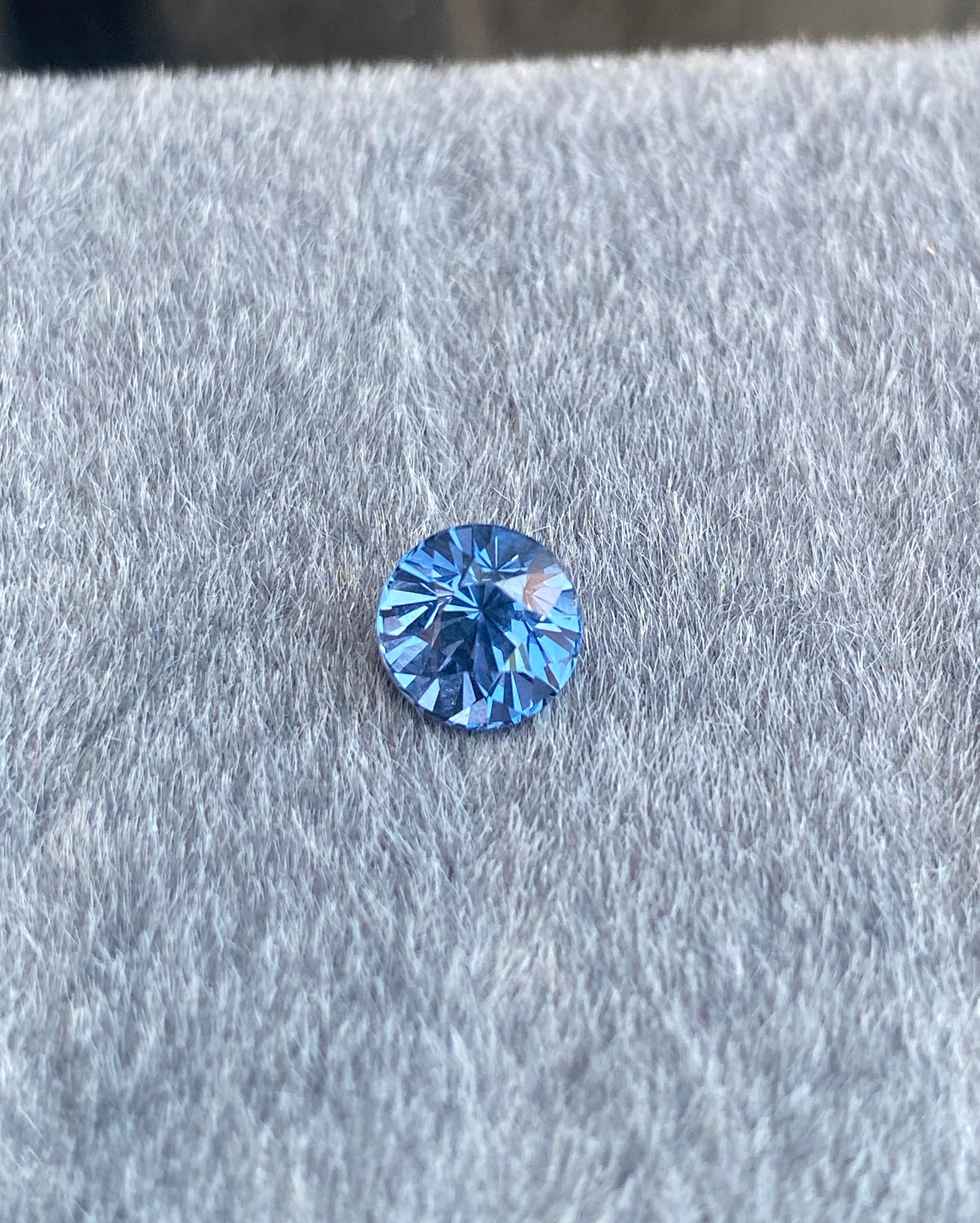 Le Spinelle Gris • 1,67 ct de Bonnot Paris, avec son design rond et taille brillant, repose sur une surface grise douce, affichant son éclat naturel à travers des facettes scintillantes.