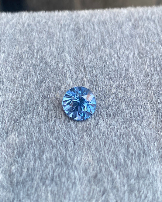 Le Spinelle Gris • 1,67 ct de Bonnot Paris, avec son design rond et taille brillant, repose sur une surface grise douce, affichant son éclat naturel à travers des facettes scintillantes.