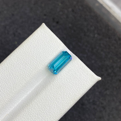 Une pierre précieuse rectangulaire taille émeraude Zircon Bleu · 4,44 ct de Bonnot Paris est présentée sur une surface texturée blanche sur un fond sombre.