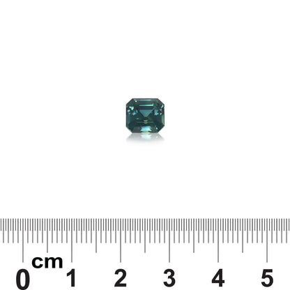 Un Saphir Teal de 3,03 ct de Bonnot Paris, une petite pierre précieuse verte facettée, est placé sur un fond blanc au-dessus d'une règle avec des mesures en centimètres, indiquant qu'il mesure environ 0,6 cm de large.