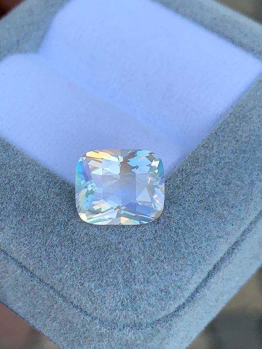 Une pierre de lune taille coussin de 3,8 carats de Bonnot Paris, affichant des couleurs irisées et des teintes pastel, est présentée sur une boîte à bijoux bleu clair ouverte.