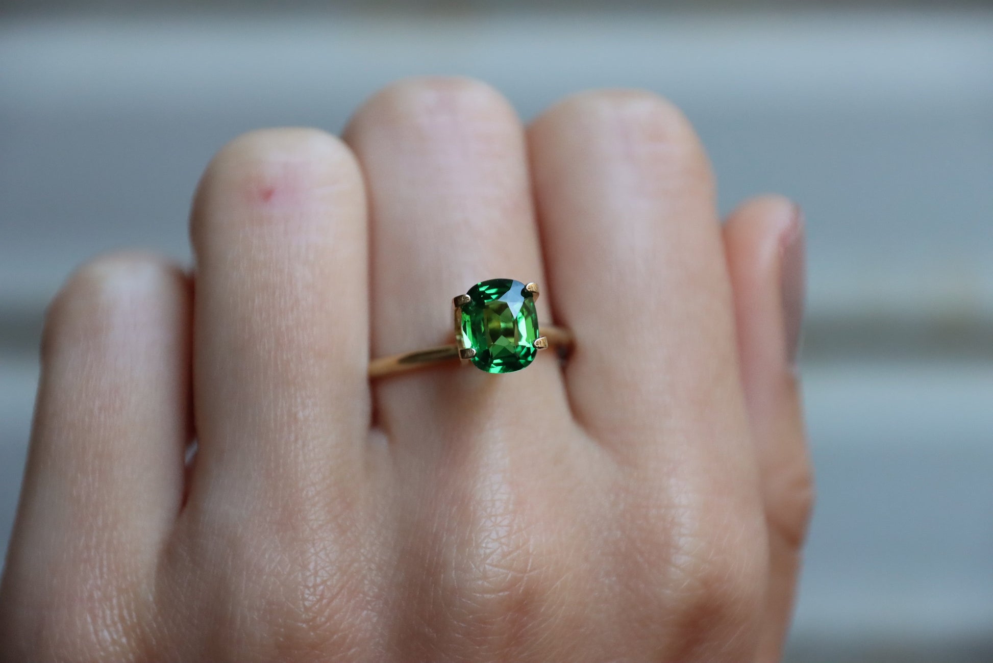 Une main présente une bague en or Bonnot Paris ornée d'une pierre précieuse Grenat Tsavorite verte ovale de 1,7 ct sur un fond neutre flou.