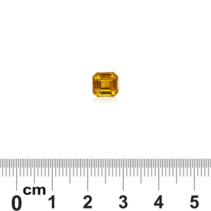 Le Saphir Jaune de 2,04 carats de Bonnot Paris, une pierre précieuse jaune de taille carrée, repose sur un fond blanc, une règle en dessous indiquant sa taille compacte. Il reflète brillamment la lumière, mettant en valeur ses facettes et sa clarté.