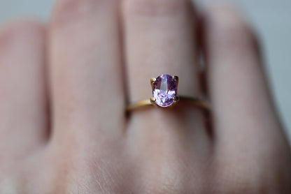 Un gros plan montre une main portant la bague Saphir Violet de Bonnot Paris, ornée d'une pierre précieuse rose taille ovale de 1,59 ct, sur l'annulaire avec un arrière-plan flou.