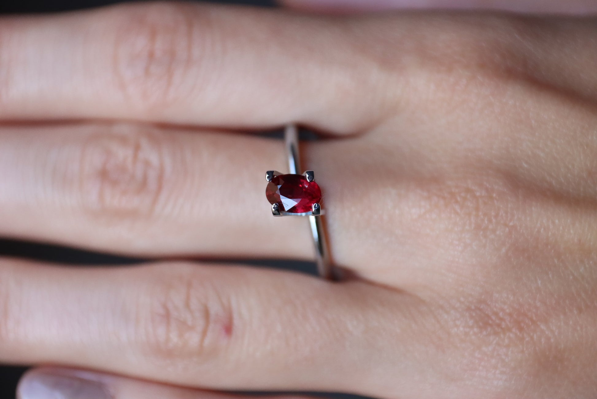 Une main portant la bague en argent Rubis du Mozambique de 1,01 ct de Bonnot Paris avec une pierre précieuse rouge de forme ovale dans un sertissage à quatre griffes, sur un fond légèrement flou.