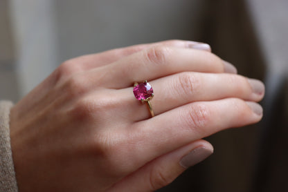 Gros plan d'une main ornée du Saphir Rose · 3,02 carats de Bonnot Paris, mettant en valeur une grosse pierre ronde rose vif. La main est ornée d'un vernis à ongles de couleur neutre sur un arrière-plan légèrement flou.