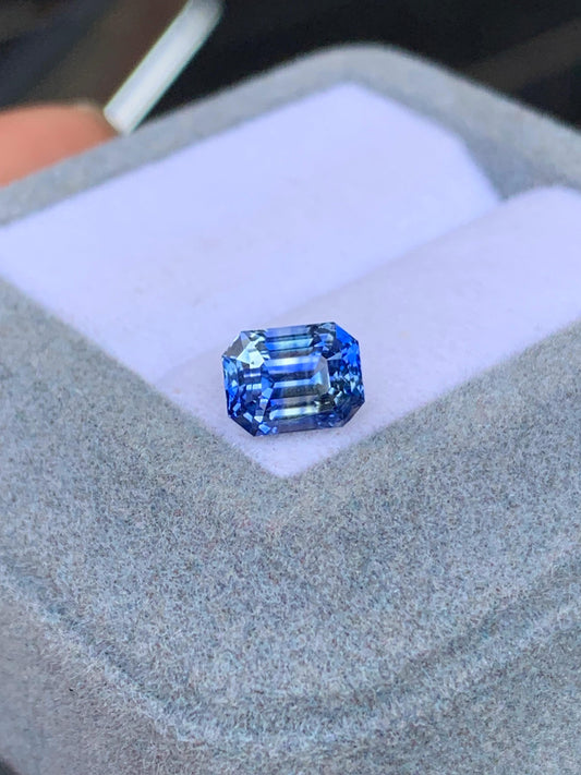 Ce superbe Saphir Bicolore de 2,06 carats du Sri Lanka par [NOUVEAU] Bonnot Paris, logé dans un coffret en velours gris avec un intérieur doux et lumineux, met magnifiquement en valeur sa clarté et sa brillance grâce à de superbes facettes taille émeraude.