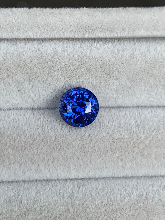 Un Saphir Bleu rond taille brillant • 2,52ct de Bonnot Paris repose sur un tissu doux et gris clair, accentuant sa couleur vive et son éclat.