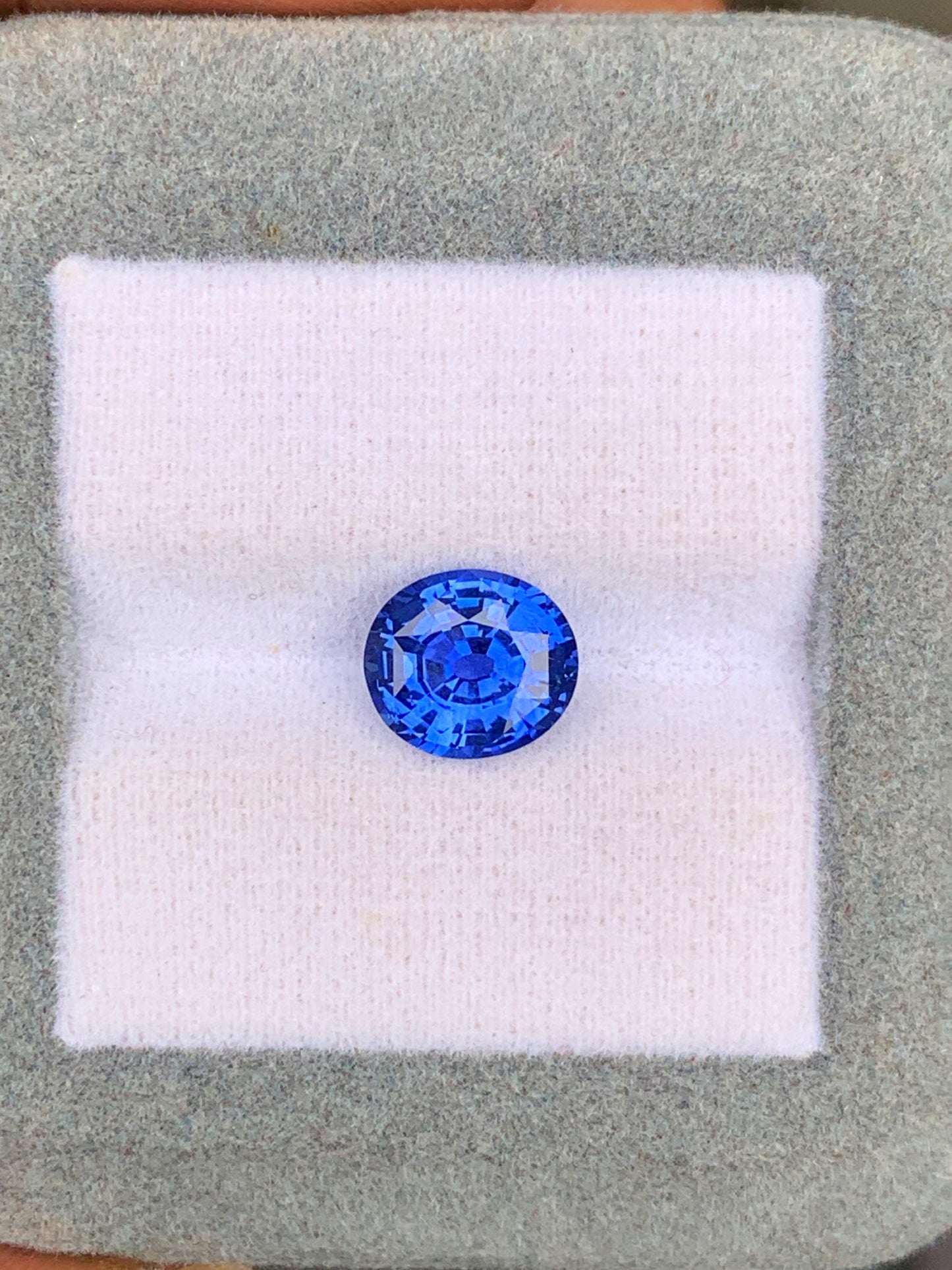 Un Saphir Bleu de 2,60 carats de Bonnot Paris, originaire du Sri Lanka, est présenté sur un fond blanc et gris, la lumière se reflétant sur ses facettes.
