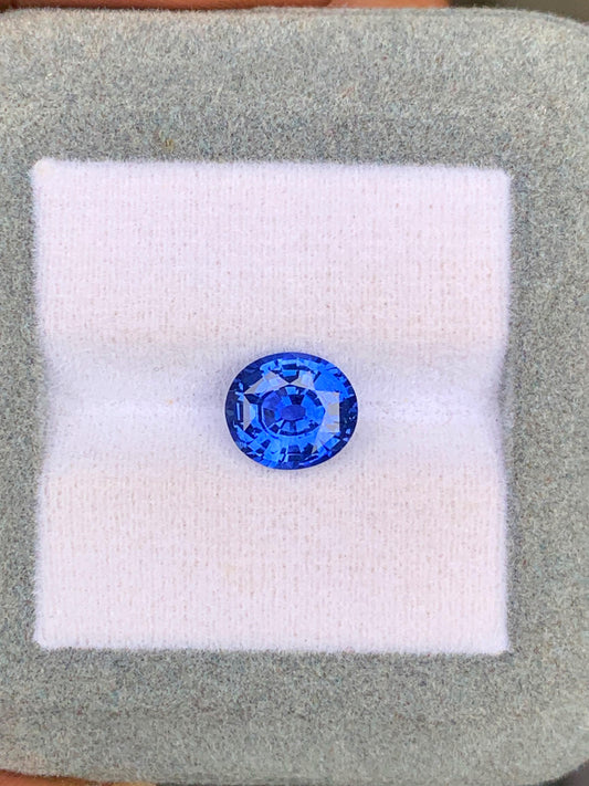 Un Saphir Bleu de 2,60 carats de Bonnot Paris, originaire du Sri Lanka, est présenté sur un fond blanc et gris, la lumière se reflétant sur ses facettes.
