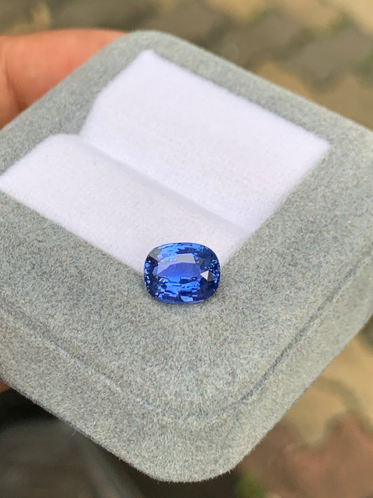 Un gros plan du Saphir Bleu · 3,05ct de [NOUVEAU] Bonnot Paris sur une boîte à bijoux gris clair avec un intérieur blanc met en valeur la couleur vibrante de la pierre précieuse taille coussin sur un fond flou.