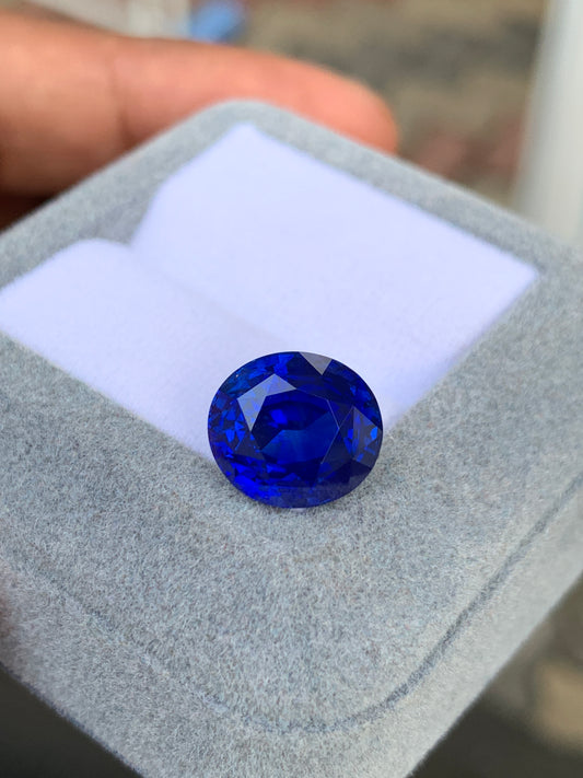 Un Saphir Bleu de 8,03 carats signé Bonnot Paris est présenté dans un écrin en feutre gris clair. La pierre ovale capture magnifiquement la lumière, révélant une palette de nuances de bleu sur un fond délicatement flou.