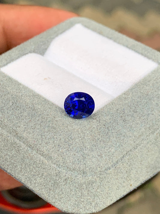 Le Saphir Bleu de 2,51 carats de Bonnot Paris [NOUVEAU] est présenté dans un écrin gris ouvert sur un coussin blanc. Sa teinte bleu profond reflète brillamment la lumière. L'attrait de cette pierre précieuse est magnifiquement mis en valeur sur un fond légèrement flou.