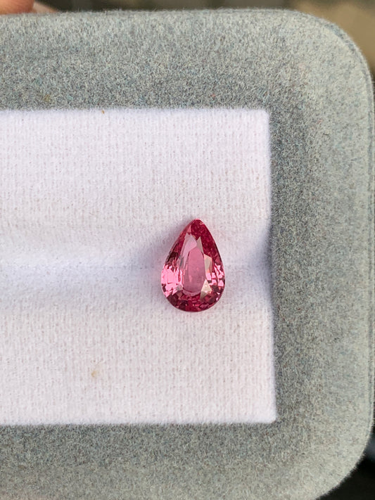 La pierre précieuse Saphir Padparadcha de 2,04 ct de Bonnot Paris présente une forme de poire et une couleur rose vibrante, élégamment présentée sur une surface texturée grise et blanche.