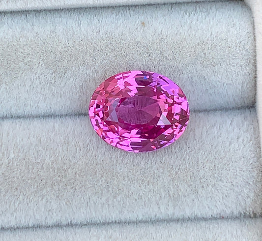 Un saphir rose ovale scintillant de 7,05 ct repose sur un fond de velours gris moelleux, mettant en valeur sa couleur vibrante et ses facettes complexes, un véritable témoignage de la rareté exceptionnelle de [NOUVEAU] Bonnot Paris.