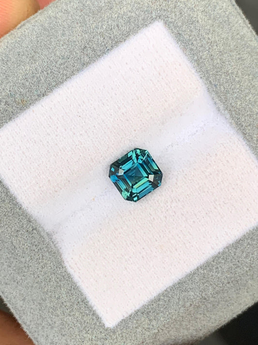 La [NOUVELLE] pierre précieuse Bonnot Paris Saphir Teal • 2,05 carats, provenant de Madagascar, est présentée dans un écrin doublé de velours gris. Ses facettes taille émeraude scintillent sous la lumière, mettant en valeur sa magnifique teinte bleu sarcelle et sa clarté.