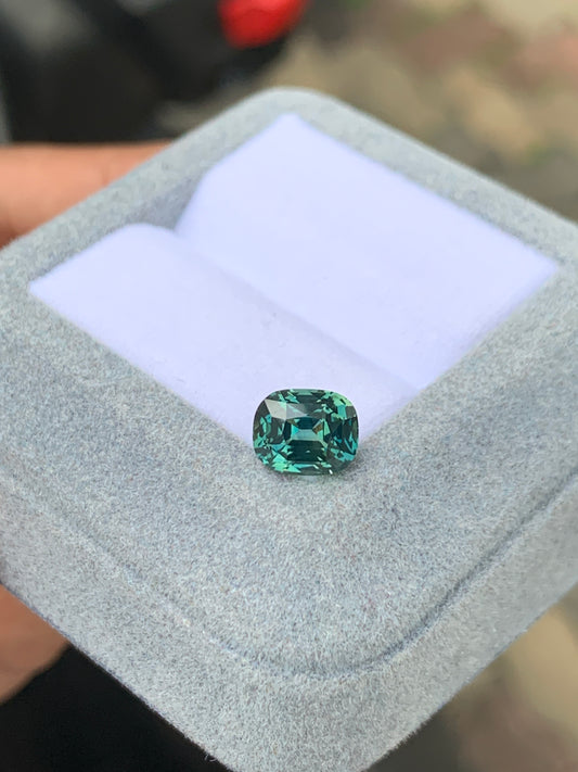 Une pierre précieuse rare Saphir Teal de 2,53 ct de [NOUVEAU] Bonnot Paris scintille de sa couleur vert foncé, reposant dans une boîte à bijoux gris clair avec une doublure blanche douce sous la lumière naturelle.