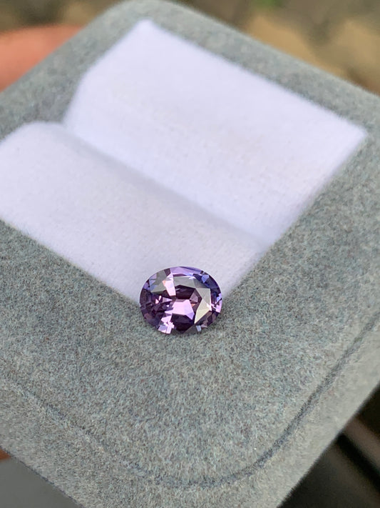 Un Saphir Violet de 1,39 ct de [NOUVEAU] Bonnot Paris se trouve dans une boîte à bijoux ouverte en velours gris, doublée de tissu blanc, ses facettes captant la lumière et présentant une teinte lavande vibrante.