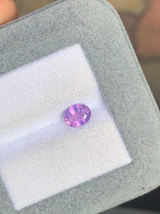 Le Saphir bicolore • 1,05ct de [NOUVEAU] Bonnot Paris, une pierre précieuse taille ovale aux allures de saphir sri-lankais, est présenté dans une luxueuse boîte en tissu gris et blanc sous un angle exquis.