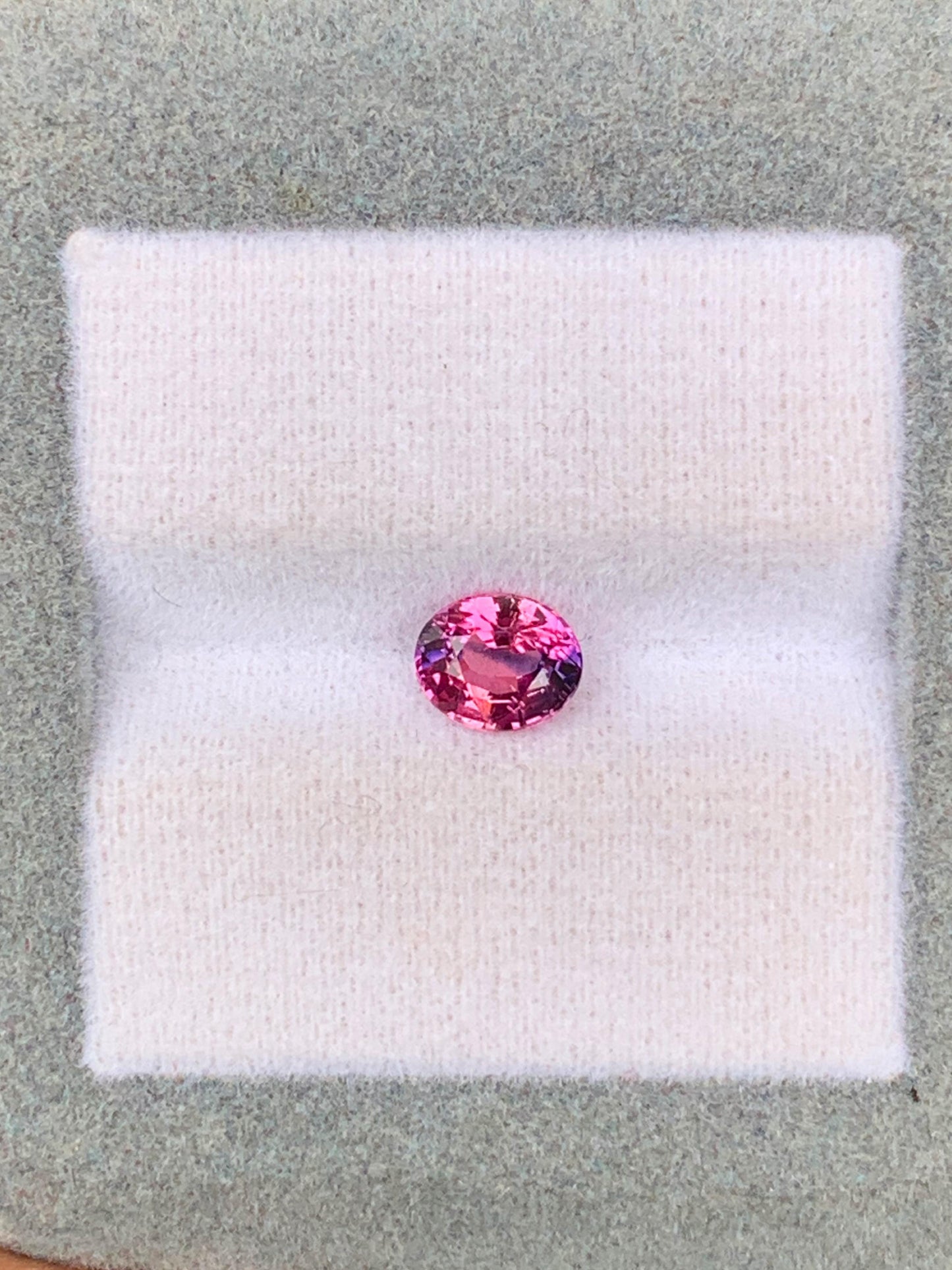 Un Saphir bicolore de 1,06 ct du Sri Lanka, par Bonnot Paris, est présenté sur un tissu blanc doux avec un cadre gris, apparaissant vibrant et réfléchissant.