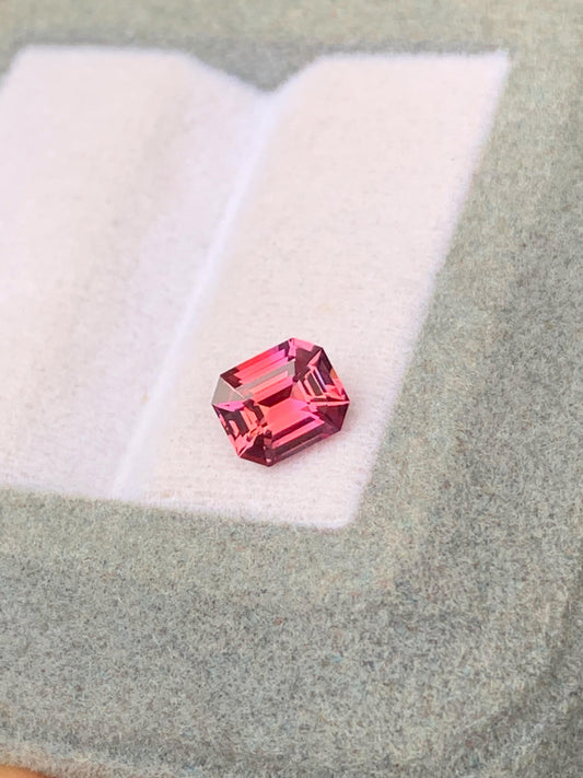 Le Saphir bicolore de 1,12 ct de Bonnot Paris, une pierre précieuse taille émeraude rose, est présenté sur une surface en feutre gris clair avec un fond doucement éclairé.