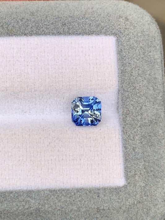 Le "Saphir bicolore" de 2,05 carats de chez Bonnot Paris repose sur un tissu léger à l'intérieur d'un écrin gris, scintillant de diverses nuances de bleu.