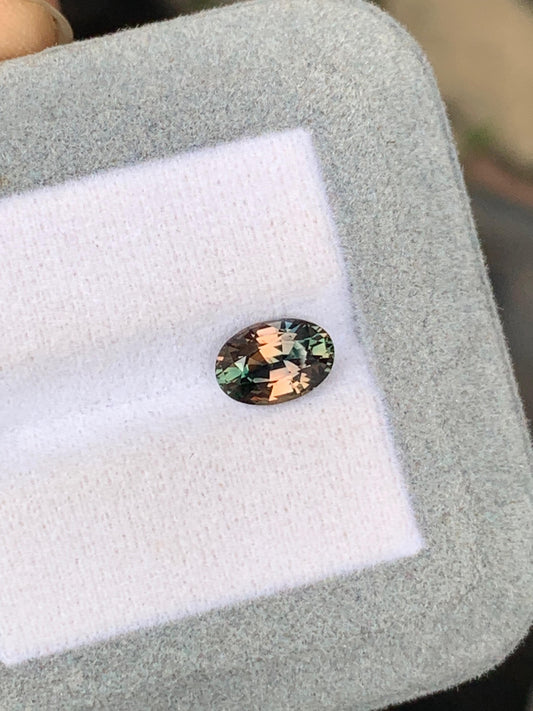 Un Saphir bicolore ovale étincelant de 2,05 ct de Bonnot Paris, aux reflets verts et roses, repose sur un support gris clair. Originaire du Sri Lanka, cette pierre précieuse reflète magnifiquement la lumière pour mettre en valeur ses facettes complexes.