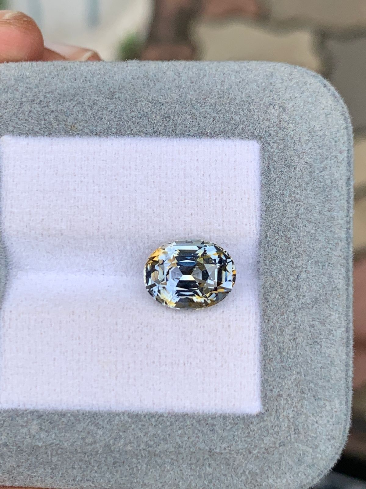 Le Saphir bicolore • 5,00ct de [NOUVEAU] Bonnot Paris est élégamment présenté dans un écrin à bijoux coussiné gris et blanc, soulignant sa clarté et sa brillance tout en captant magnifiquement la lumière.
