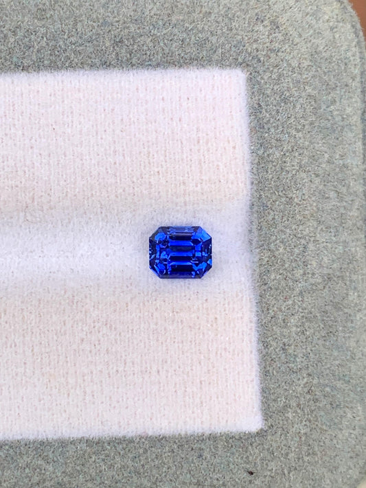 Le Saphir bleu • 1,02ct de [NOUVEAU] Bonnot Paris est une gemme taille émeraude du Sri Lanka, reposant sur un doux tissu blanc et gris, mettant en valeur ses facettes claires et sa riche couleur bleue.