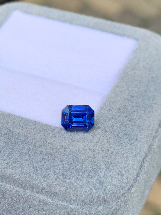 Le Bonnot Paris Saphir bleu • 1,03ct est une pierre précieuse taille émeraude à la teinte vibrante, élégamment présentée dans un coffret à bijoux gris clair avec un intérieur en mousse blanche, mettant en valeur ses facettes uniques.