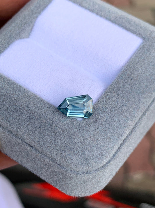 Le Saphir bleu Bonnot Paris • 1,59ct, une pierre précieuse bleue étincelante avec une taille géométrique angulaire, est magnifiquement niché dans un coffret à bijoux en velours gris avec un intérieur blanc.