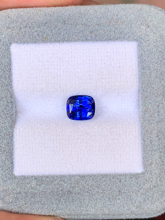 Un saphir bleu taille coussin de 2,03 carats du Sri Lanka par Bonnot Paris repose sur un tissu blanc dans une boîte à bijoux grise.