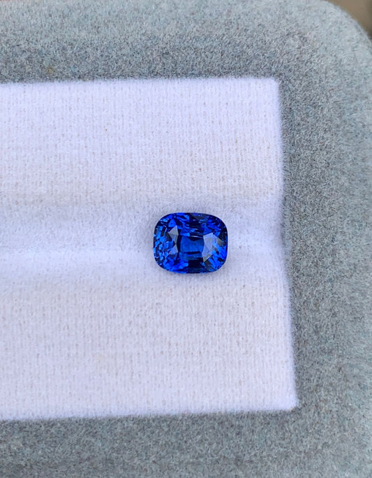 Un saphir bleu taille carrée de 2,05 carats de Bonnot Paris est élégamment présenté sur une surface texturée blanche et grise, mettant en valeur sa couleur vive et ses facettes. Cette gemme d'exception captive par sa beauté rappelant les plus beaux trésors du Sri Lanka.