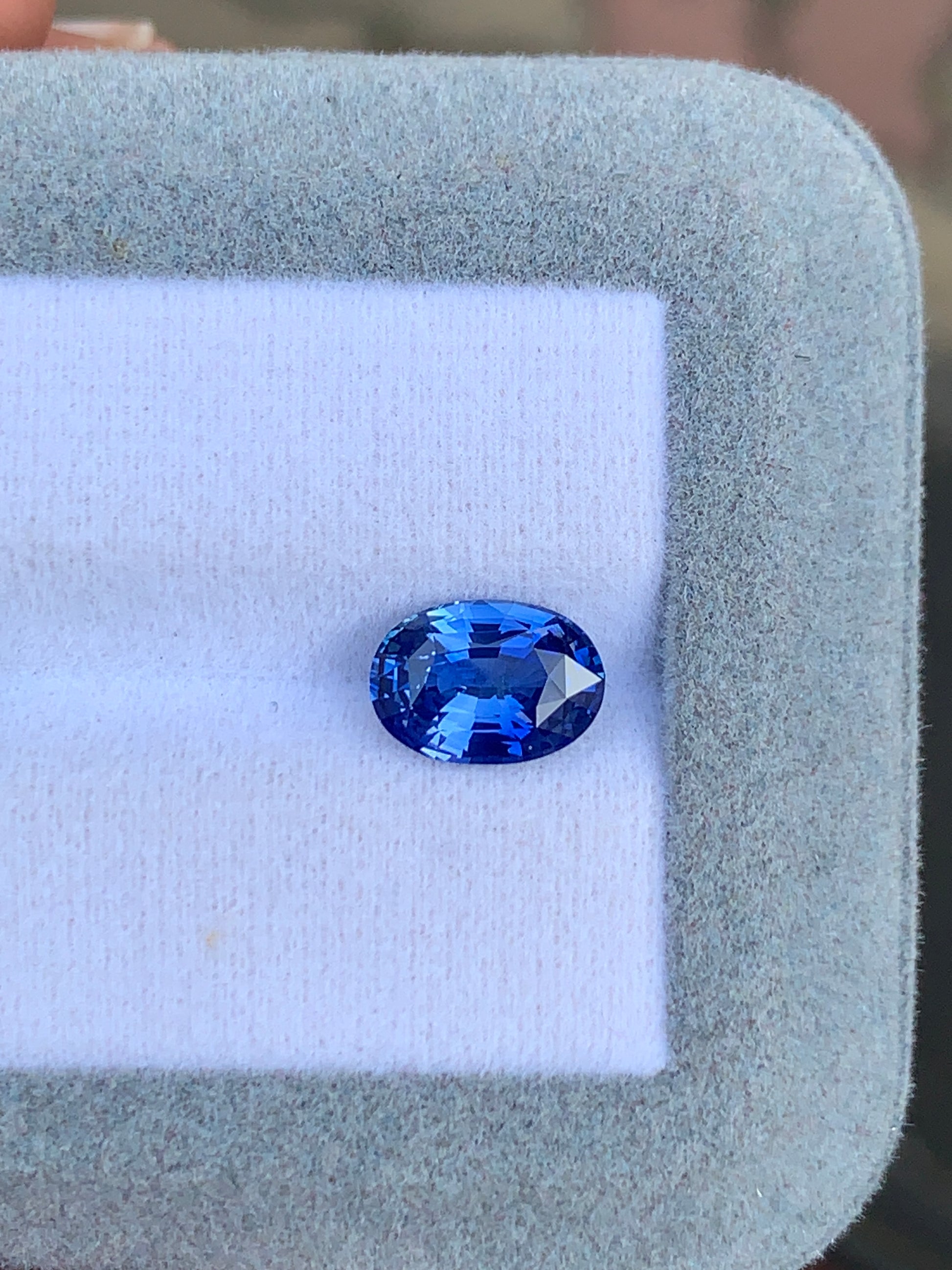 Un Saphir bleu de 2,51 carats de Bonnot Paris brille de mille feux sur une surface coussinée blanche, entourée d'un tissu gris clair, soulignant son allure exquise.